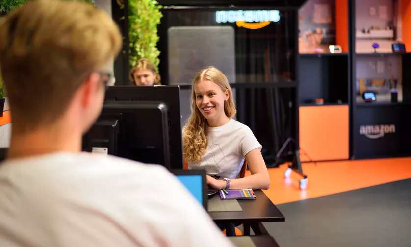 Studentka siedzi przy komputerze i patrzy w obiektyw aparatu.