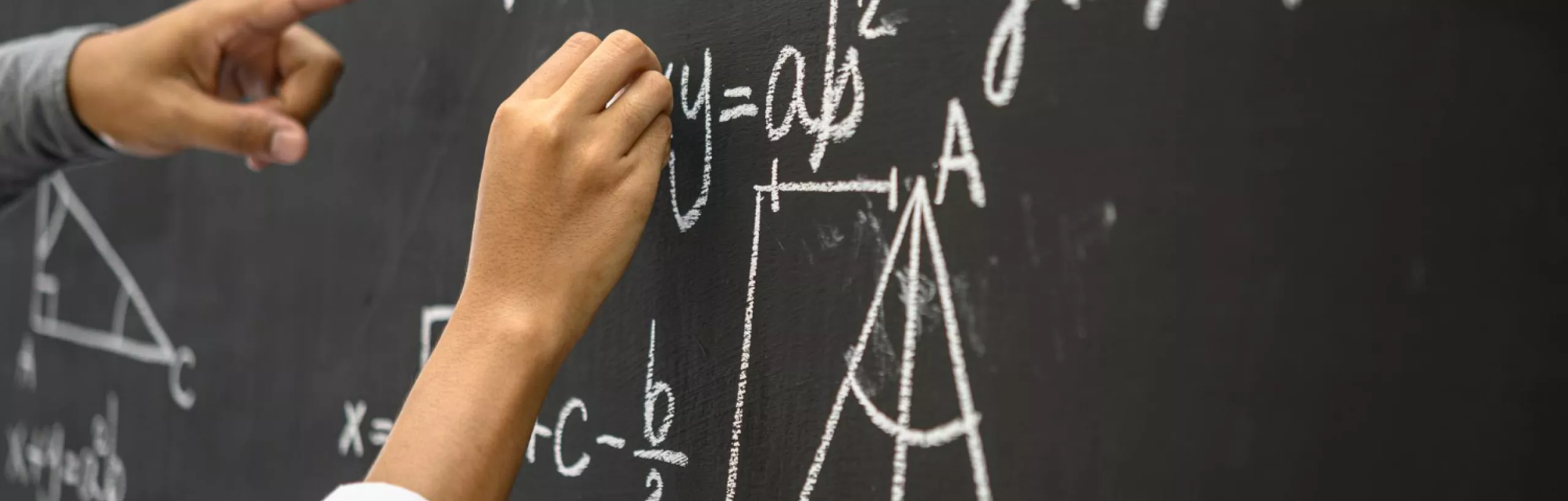 Ręka pisząca na tablicy wzory matematyczne.