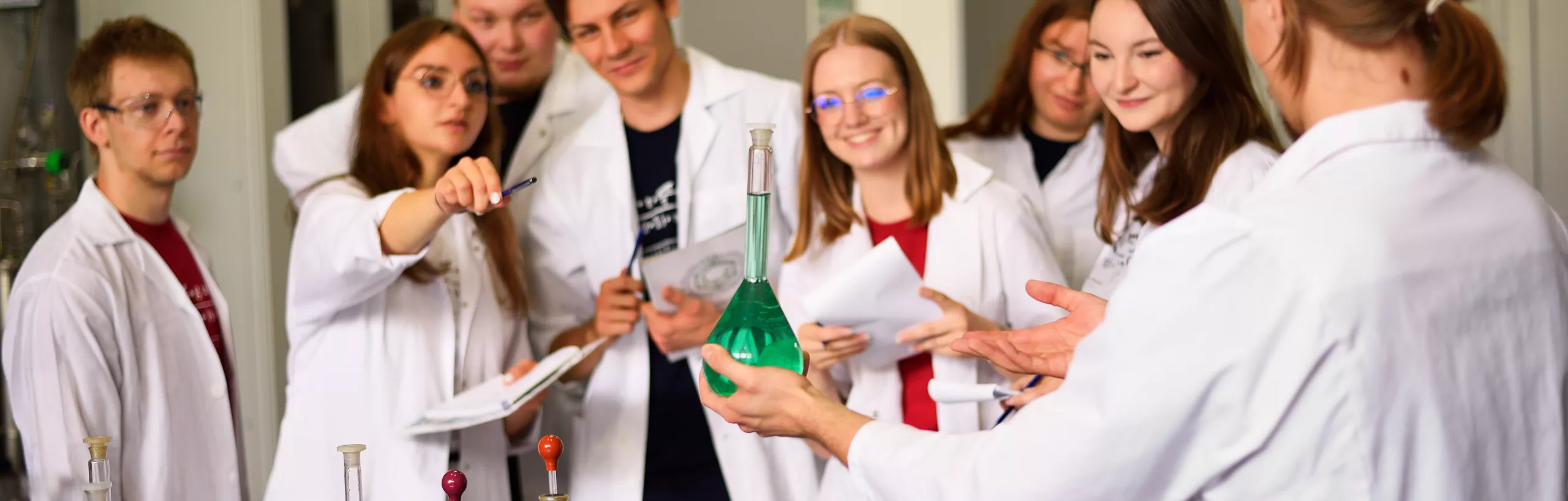 Studenci w laboratorium oglądają preparat chemiczny.