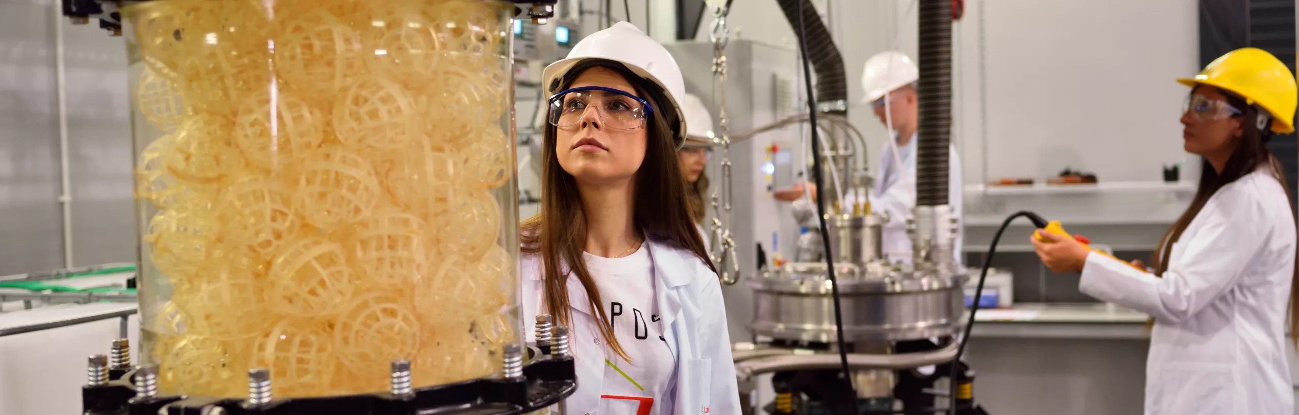 Studenci patrzą na żółte kule w hali przemysłowej.