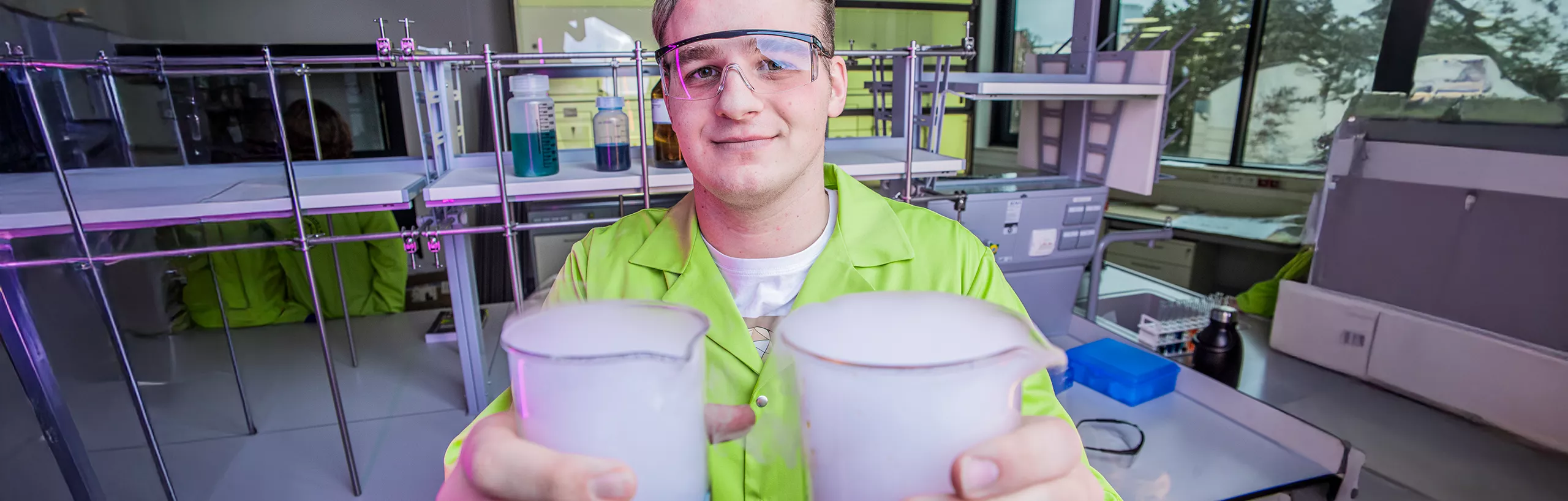 Student stoi z kolorowymi probówkami w laboratorium.